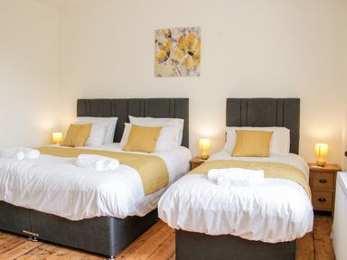 A bedroom with two beds each with white bedding yellow pillows and runners and bedside tables with lamps at The Farm in Presteigne