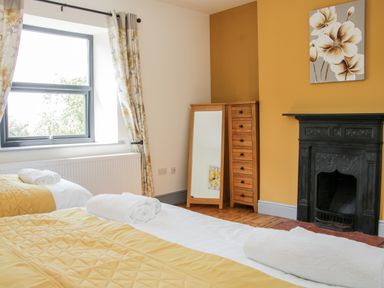 A bedroom with two beds with yellow covers rolled towels window with floral curtains wooden floor and a black fireplace at The Farm in Presteigne