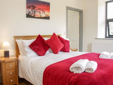 A bedroom with a bed red pillows and blanket bedside tables with lamps and a window at The Farm in Presteigne