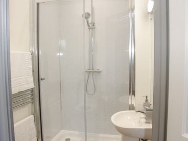 A bathroom with a glass shower enclosure a showerhead a white sink with a faucet and soap dispenser and a towel rack with white towels at The Farm in Presteigne