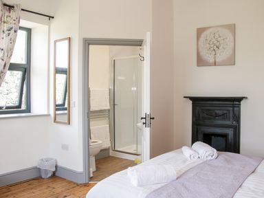 A bedroom with a bed with towels on it a black fireplace a window with floral curtains a mirror and an open door leading to a bathroom at The Farm in Presteigne