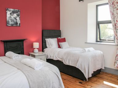 A bedroom with two single beds a red accent wall a window and a nightstand with a lamp at The Farm in Presteigne