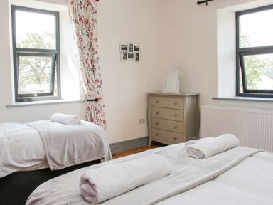 A bedroom with two beds rolled towels on each bed a chest of drawers with a mirror and two windows at The Farm in Presteigne