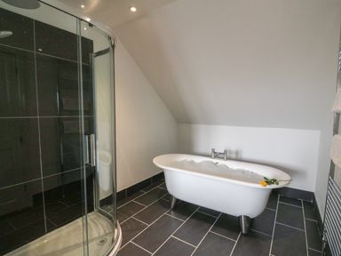 A bathroom with a clawfoot bathtub filled with bubbles and a curved glass shower enclosure at Oakwood House in Rhayader
