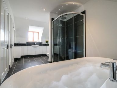 A bathroom with a filled bathtub a glass shower cubicle and a sink with a window above at Oakwood House in Rhayader