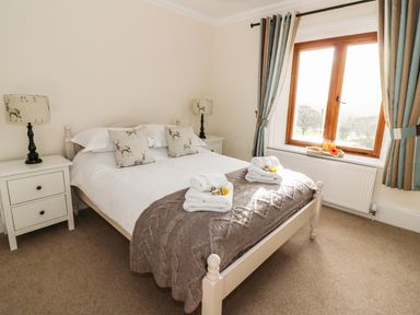 A bedroom with a bed bedside tables and lamps with deer pattern curtains and a window at Oakwood House in Rhayader