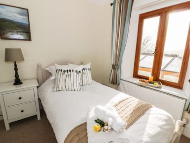 A bedroom with a single bed next to a window with curtains and a nightstand with a lamp at Oakwood House in Rhayader