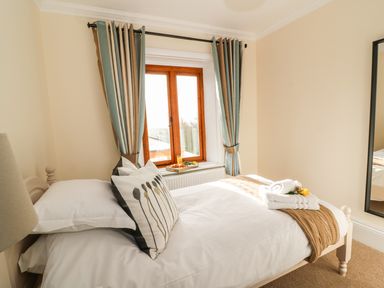 A bedroom with a single bed next to a window with curtains and a mirror on the wall at Oakwood House in Rhayader