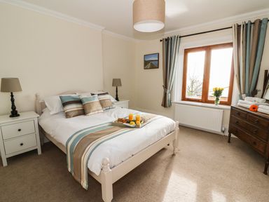 A bedroom with a bed, bedside tables with lamps, a window with curtains, and a wooden dresser with towels and flowers at Oakwood House in Rhayader