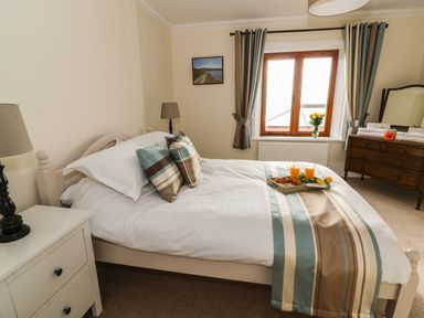 A bedroom with a bed with striped bedding and pillows a nightstand with a lamp a window with curtains and a dresser with towels and flowers at Oakwood House in Rhayader