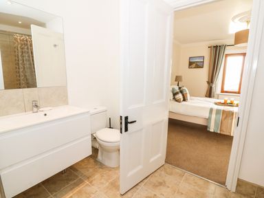 A bathroom with sink and toilet visible next to a bedroom with a bed and window at Oakwood House in Rhayader