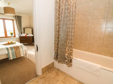 A bedroom with a bed and dresser seen through the doorway of a bathroom with a tiled bathtub and shower curtain at Oakwood House in Rhayader