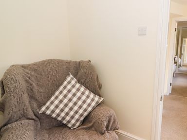 A corner with an armchair covered in a knitted throw and a checkered cushion in a hallway at Oakwood House in Rhayader