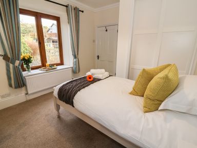 A bedroom with a bed with yellow pillows and folded towels near a window with curtains at Oakwood House in Rhayader