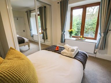 A bedroom with a bed folded towels and a flower on the bed a window with curtains and a tray of breakfast on the windowsill at Oakwood House in Rhayader