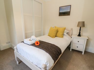 A bedroom with a single bed with yellow pillows white bedside table with a lamp and a framed picture on the wall at Oakwood House in Rhayader