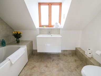 A bathroom with a bathtub a sink window with rolled towels and toilet rolls at Oakwood House in Rhayader