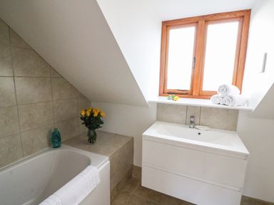 A bathroom with a bathtub a sink a window rolled towels and a vase of yellow flowers at Oakwood House in Rhayader