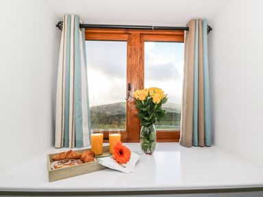 A breakfast tray with pastries and orange juice on a white table by a window with curtains and a vase of yellow roses at Oakwood House in Rhayader