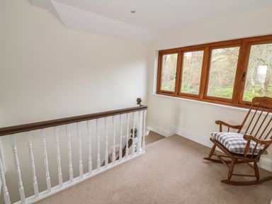 A stair landing with a wooden rocking chair holding a cushion next to a window with a view of trees at Oakwood House in Rhayader