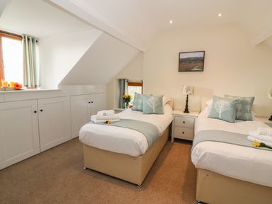 A bedroom with two single beds a nightstand between the beds and built in cupboards under a sloped ceiling at Oakwood House in Rhayader