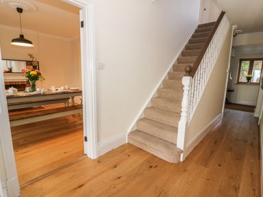 A hallway with wooden floor leading to a carpeted staircase and a dining room with a table set for tea at Oakwood House in Rhayader