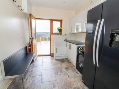 A utility room with a black bench a washing machine white cabinets a black refrigerator and a door opening to an outdoor area at Oakwood House in Rhayader