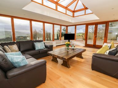 A living room with large windows wooden coffee table and brown sofas at Oakwood House in Rhayader