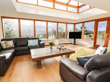 A living room with leather sofas a wooden coffee table and large windows at Oakwood House in Rhayader