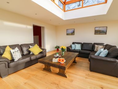 A living room with three dark sofas and a wooden coffee table under a skylight at Oakwood House in Rhayader