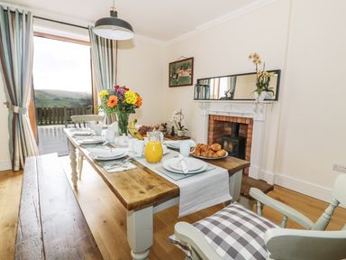 A dining room with a wooden table set for breakfast and a fireplace at Oakwood House in Rhayader