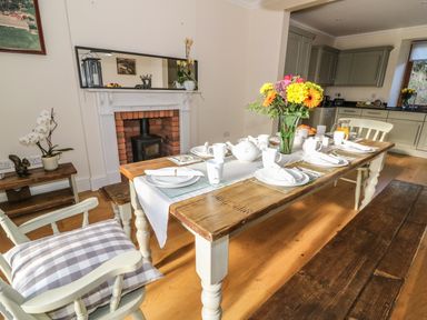 A dining room with a wooden table set for breakfast with flowers and kitchen cabinets in the background at Oakwood House in Rhayader