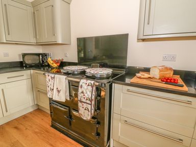 A kitchen with a black stove and oven two ovens a microwave a bowl of bananas and grapes a chopping board with bread and cherry tomatoes at Oakwood House in Rhayader