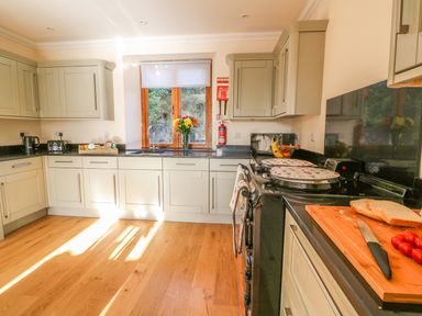 A kitchen with light-colored cabinets wooden floor and a window with flowers on the counter at Oakwood House in Rhayader