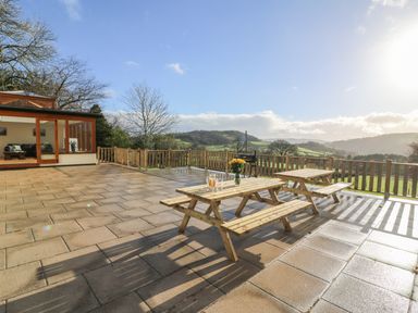 A large outdoor patio with wooden picnic tables and a railing overlooking hills at Oakwood House in Rhayader
