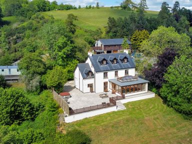 A house with a glass conservatory and large patio surrounded by trees and grass at Oakwood House in Rhayader