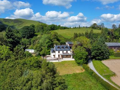 A countryside house surrounded by trees and green hills with a driveway at Oakwood House in Rhayader