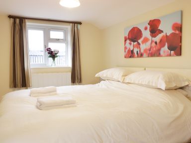 A bedroom with a white bed and folded towels on the bed near a window with curtains and a flower vase at Broadway Lands Farm in Little Dewchurch