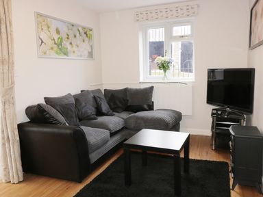 A living room with a gray sectional sofa a black coffee table a television on a stand and a window with flowers at Broadway Lands Farm in Little Dewchurch