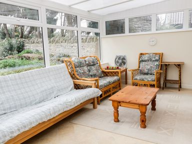 A conservatory with wooden furniture including a sofa, armchair, table, and side table at Broadway Lands Farm in Little Dewchurch