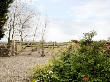 A gravel driveway with a wooden gate and trees at Broadway Lands Farm in Little Dewchurch