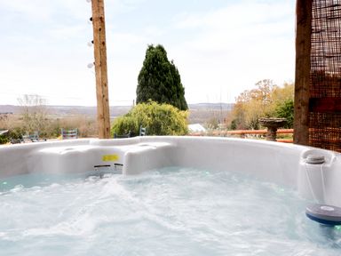 An outdoor hot tub with bubbling water under a wooden pergola overlooking trees and hills at Broadway Lands Farm in Little Dewchurch
