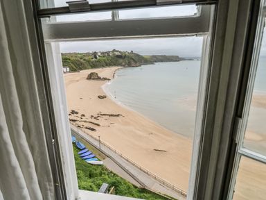 A view of a sandy beach with blue boats lined up on grass seen through a window at Apartment 3 Tenby