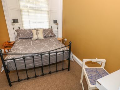 A bedroom with a black metal bed frame a gray bedspread and a white chair with patterned upholstery at Apartment 3 in Tenby