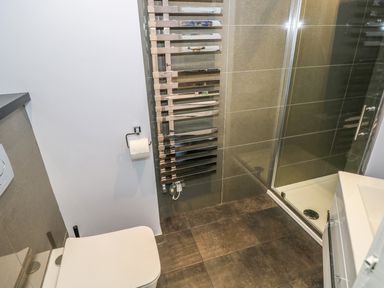 A bathroom with a toilet a wall-mounted chrome towel warmer a shower enclosure and a sink at Apartment 3 in Tenby