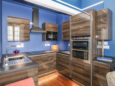 A kitchen with blue walls wooden cabinets a double oven a microwave and a sink at Apartment 3 in Tenby
