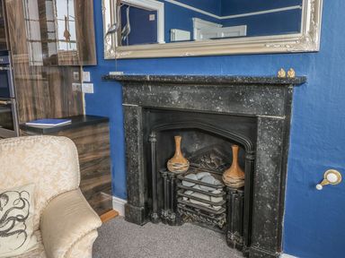 A room with a black fireplace two vases on the hearth and a beige armchair with a cushion at Apartment 3 in Tenby