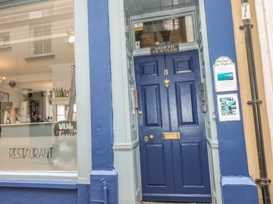 A blue door with the number 3 and a sign above it next to a window displaying part of a restaurant interior at Apartment 3 in Tenby
