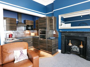 A kitchen with wood cabinets and black fireplace next to brown leather sofa at Apartment 3 in Tenby
