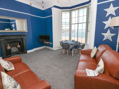 A living room with two brown sofas a small dining table by a bay window and a fireplace at Apartment 3 in Tenby